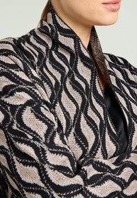 Gebreid jasje met een golfpatroon in beige en zwart, met een gestructureerde stof met metallic draden en een hoog kraagontwerp.