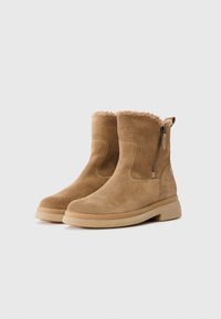 Tan suède enkellaarsjes met een pluizige, bontgevoerd bovenrand, een zijrits en een beige rubberen zool. Glad oppervlak en afgeronde neus.