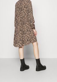 Leopardenmuster Kleid in Beige und Schwarz, mit langen Ärmeln und lockerer Passform. Getragen mit schwarzen Schnürstiefeletten.