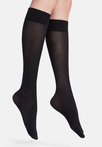 Calze nere fino al ginocchio con una fascia superiore a coste, realizzate in un materiale liscio e trasparente, dalla forma aderente e costruzione senza cuciture.