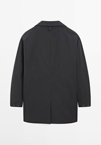 Cappotto nero non foderato con yoke posteriore, maniche lunghe, polsini con bottone e taglio dritto. Il materiale sembra liscio con una finitura opaca.