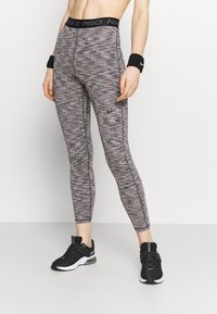 Legíny Nike Pro v černé a šedé melírované vzoru, přiléhavý střih, vysoký pas s logem, spárované s černými sportovními botami.
