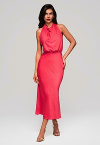 Robe sans manches rose avec un col halter, dotée d'un bustier drapé et d'une taille ajustée. Jupe longue et fluide avec une texture lisse et un léger éclat.