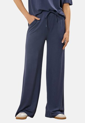 Granatowe spodnie o szerokich nogawkach z troczkiem, noszone z białymi i beżowymi trampkami, ręce spoczywają w kieszeniach i wzdłuż ciała.