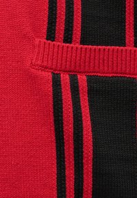 Κοντινό πλάνο κόκκινου και μαύρου πλεκτού υφάσματος με κάθετες ρίγες και οριζόντια ριγέ λωρίδα στο κέντρο.