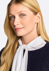 Maglione a maglia navy con scollatura rotonda, impreziosito da una sciarpa bianca annodata davanti. Capelli biondi lunghi e lisci. Tonalità di pelle morbida e naturale.