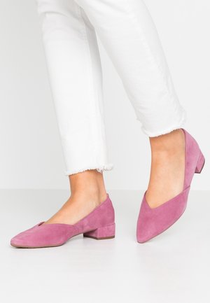 Różowe zamszowe buty na słupku z ostrym noskiem i otwartymi bokami, noszone z białymi, ściętymi dżinsami z postrzępionymi brzegami.