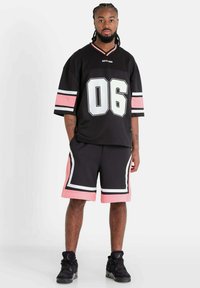 Jersey deportivo negro con el gran número blanco "06", mangas a rayas rosas y blancas, combinado con pantalones cortos negros con acentos rosas y ribete blanco.