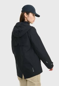 Veste étanche noire avec capuche, marquage Gore-Tex et poignets ajustables. Comprend une ventilation arrière et un design moderne et épuré.