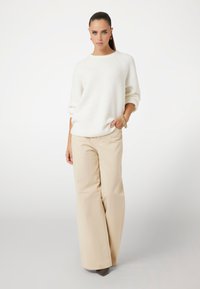 Pull en maille blanche chunky avec des manches raglan associé à un pantalon large beige, présentant une texture lisse et des détails de couture subtils.