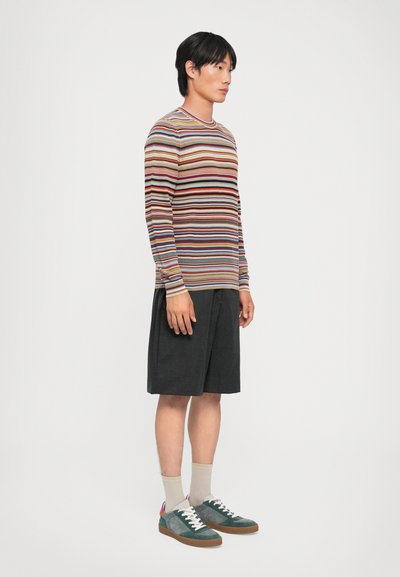 Chemise à rayures à manches longues dans différentes couleurs, associée à un short sombre. Le footwear se compose de suède vert, de lacets blancs et d'accents contrastants.