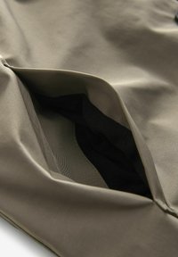 Buzunar din țesătură de culoare verde olive cu o căptușeală moale de culoare neagră, având o textură netedă și marginile curate, destinat stocării într-un articol de îmbrăcăminte.