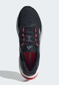 Zapatillas deportivas negras con parte superior de malla transpirable, acentos rojos, un collar acolchado y una suela de goma texturizada con detalle de logo.