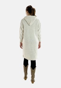 Cardigan con cappuccio lavorato a maglia in beige chiaro con un motivo testurizzato, maniche lunghe e spacchi laterali, abbinato a leggings neri e stivali cowboy color cammello.