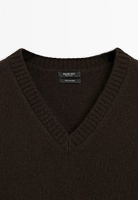 Dark brown cashmere sweater with a V-neck design. Features ribbed edges at the neckline. Label includes brand and fabric care details.
