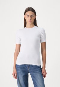 Hvit ribbestrikket kortermet t-skjorte med rund hals, tettsittende silhuett og glatt tekstur. Kombinert med blå denimjeans.