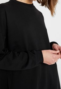 Felpa nera a maniche lunghe in un tessuto liscio, con scollatura rotonda e vestibilità rilassata. Polsini larghi e dettagli sulle cuciture laterali.
