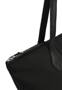 Bolsa tote negra con un cuerpo de tejido texturizado, acentos de cuero, cierre con cremallera y dos asas. Presenta un diseño elegante y angular.