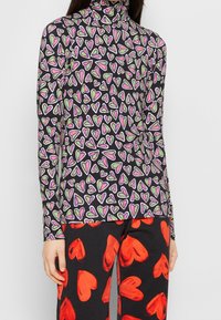 Långärmad topp med svart bakgrund och ett flerfärgat hjärtmönster i rosa, röd och grön. Design med hög hals och mjuk textur.