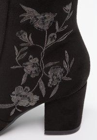 Bottine en daim noir avec talon épais et broderie florale grise sur le côté.