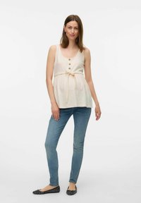 Ljusbeige ärmlös topp med rundad halsringning, dekorativa knappar och ett band vid midjan, kombinerad med blå skinny jeans och svarta ballerinas.