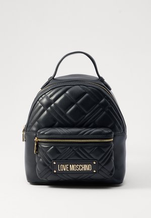 Black leather backpack with quilted pattern, gold hardware, and a front zip pocket featuring a branded plaque. Rounded shape, dual zip closure.