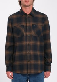 Button-up flannel shirt with dark blue and brown plaid pattern. Features two chest pockets and green buttons. Soft fabric with long sleeves.