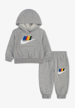 Szary zestaw dla malucha Nike z bluzą z kapturem i spodenkami dresowymi z wielokolorowym logo Nike i białym znakiem Swoosh na przodzie obu elementów.