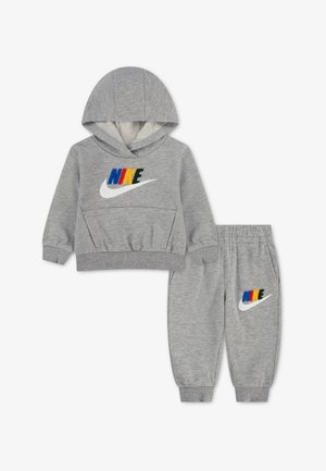 Szary zestaw dla malucha Nike z bluzą z kapturem i spodenkami dresowymi z wielokolorowym logo Nike i białym znakiem Swoosh na przodzie obu elementów.