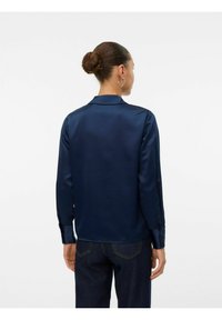Marinblå satin långärmad skjorta med krage, button-cuffs och en slät yta. Buren med mörka denimjeans, vilket visar en enkel design.