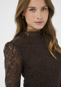 Rochie din dantelă maro cu un guler înalt, mâneci bufante și modele florale complicate, având o textură transparentă și un decolteu detaliat.