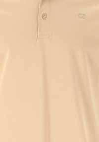 Beige polo-paita, joka on valmistettu teksturoidusta kankaasta ja jossa on kolmen napin etumus sekä hillitty logo vasemmassa rinnassa. Perinteinen istuvuus.