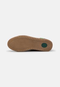 Brown rubber shoe sole with a wavy pattern, featuring a green logo accent. Smooth texture with a rounded shape.