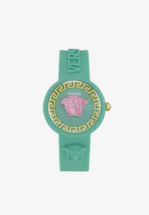 Montre en caoutchouc vert menthe avec un emblème Méduse rose, des accents dorés et un motif grec decoratif autour du cadran. Présente un bracelet texturé.