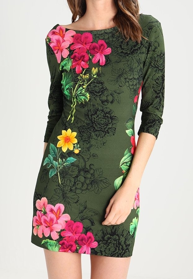 Femme portant une robe ajustée vert foncé à manches trois-quarts avec des motifs floraux rose vif, rouge et jaune.
