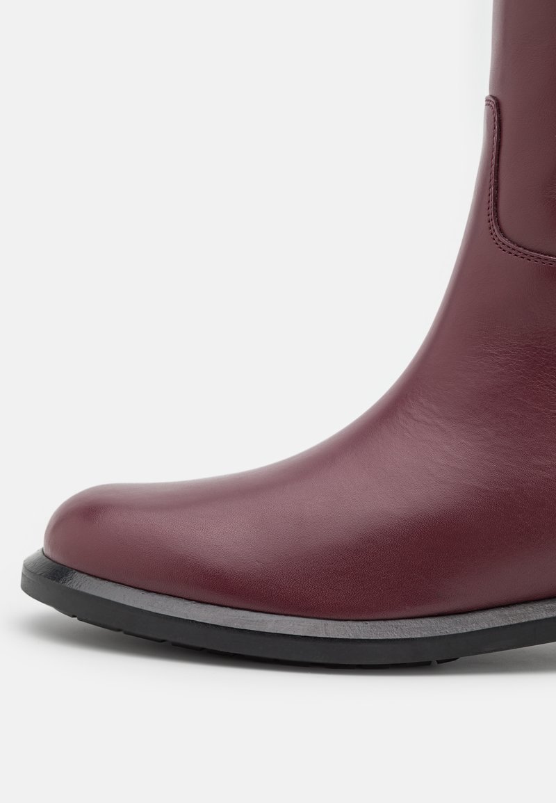 Burgunderfarbene Leder-Ankle-Boots mit runder Zehenpartie, matter Oberfläche und minimalistischem Design. Verfügt über eine schwarze Gummisohle für Langlebigkeit.