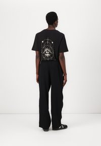 T-shirt noir avec un design graphique blanc au dos, associé à un pantalon noir ample et des baskets noires. Style simple et décontracté.