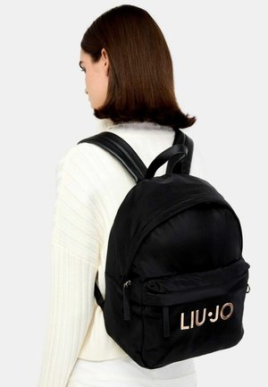 Zaino in nylon nero con forma arrotondata, due spallacci regolabili e una tasca frontale con logo dorato. Tessuto liscio con dettagli minimi.