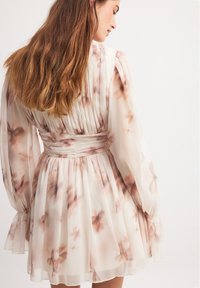 Lahka cvjetna haljina od prozirnog, lepršavog materijala s dugim rukavima i strukiranim strukom. Sadrži pregibne detalje i rašireni suknju.