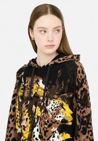 Haut de survêtement à capuche avec un design audacieux en imprimé léopard noir, marron et jaune, doté d'une texture douce et de cordons de serrage réglables.