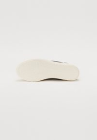 Baskets noires avec une semelle en caoutchouc texturée, dotées d'un intermédaire blanc et d'un motif hexagonal. Le design est minimaliste, sans logos visibles.