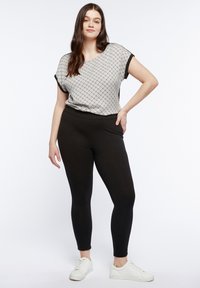 Leggings neri abbinati a una maglietta a maniche corte con un motivo geometrico in bianco e nero. L'outfit comprende sneakers bianche.