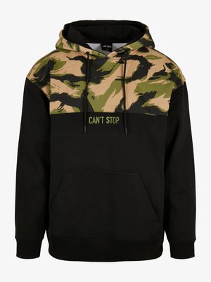 Sweat à capuche avec un corps noir et un motif de camouflage vert et beige sur le dessus. L'avant affiche le texte "CAN'T STOP" en vert.
