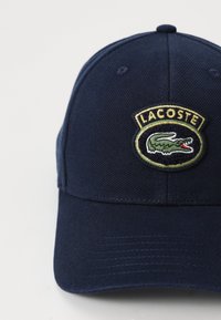 Casquette de baseball en coton bleu marine avec un visière incurvée, comportant un logo Lacoste brodé en vert, blanc et rouge à l'avant.