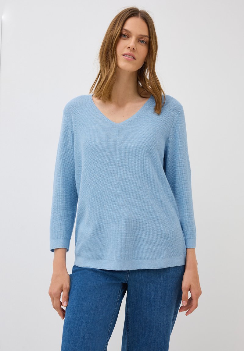 Helles blaues V-Ausschnitt-Sweatshirt mit einem strukturierten Strickmuster, 3/4-Ärmeln und einer lockeren Passform, kombiniert mit blauen Jeans.
