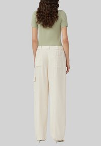 Jasnozielona bluzka krótki rękaw w połączeniu z luźnymi, kremowymi spodniami cargo z bocznymi kieszeniami i wykończeniem o teksturze.