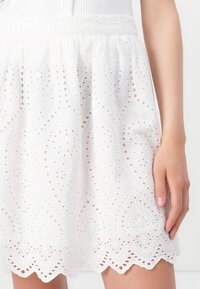 White embroidered skirt featuring intricate cut-out patterns, scalloped hem, and a gathered elastic waistband. Soft, lightweight fabric.