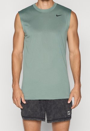 Man draagt een mouwloos groen Nike trainingsshirt en zwarte sportshorts, staand met ontspannen armen langs het lichaam.