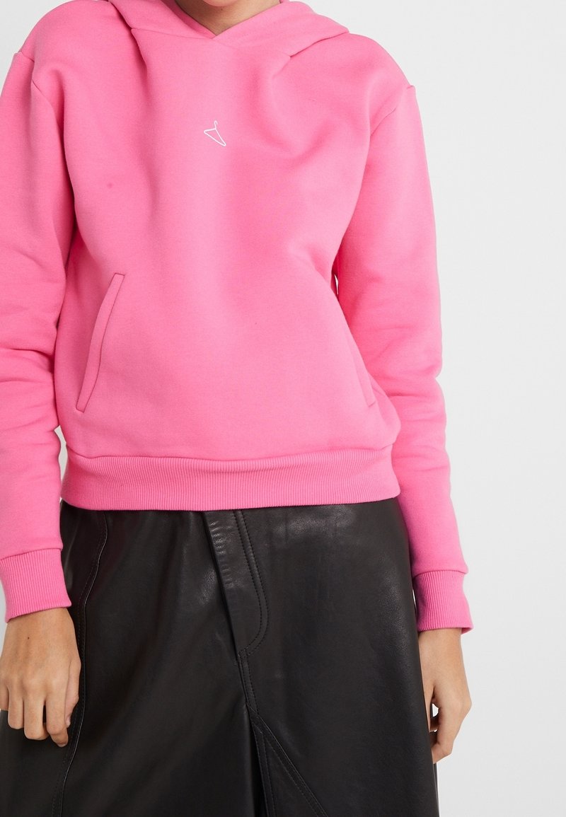 Sudadera rosa con capucha, bolsillo delantero y puños acanalados, combinada con una falda de cuero negra que presenta un detalle de costura frontal.