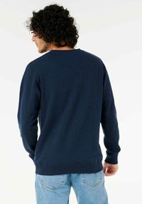 Navy blue crew neck sweatshirt with long sleeves, made of soft fabric, featuring ribbed cuffs and hem, worn with light blue jeans.